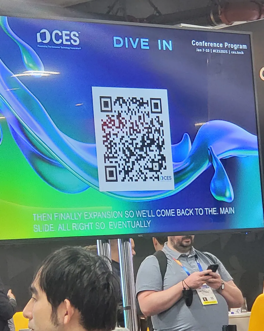 Un écran du CES à Las Vegas affiche le programme des conférences, des visiteurs devant.